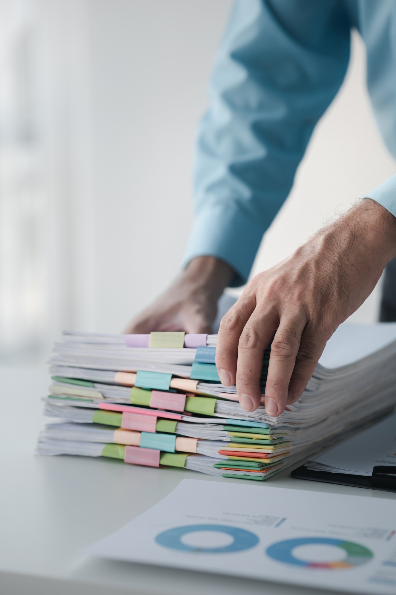 A person in an office with a huge stack of papers, he is a company employee, managing paperwork and